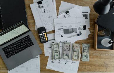 Laptop, calculator, spreadsheets, and cash on a desk, representing financial analysis and planning workspace